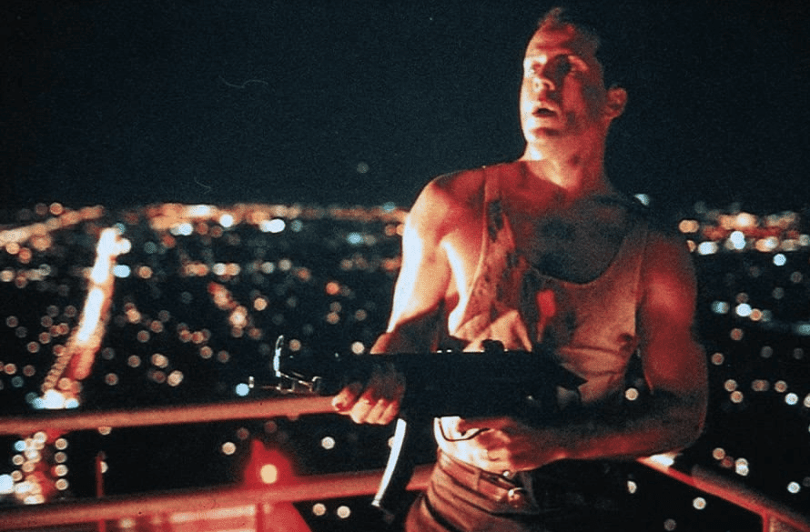 John stands on the rooftop of the Nakatomi building with a gun.